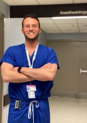 Deburghgraeve stands with a smile on his face, dressed in his scrubs inside of the ICU.