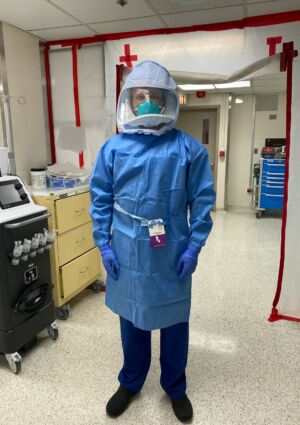 Cory Deburghgraeve stands in the ICU wearing his full PPE.  Multiple gloves, a full protective gown, an N-95 mask, and a full face shield.