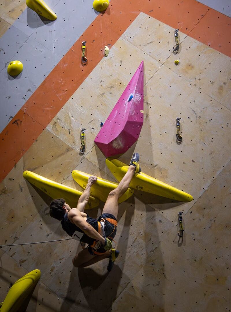 Austin Reitz hangs onto the wall by his heel as he chalks up and gets ready to pull on his heel to make the next move at the Beast Fingers League (BFL) climbing competition at Longmont Climbing Collective in August 2026. (Photo by Harley Parsons)