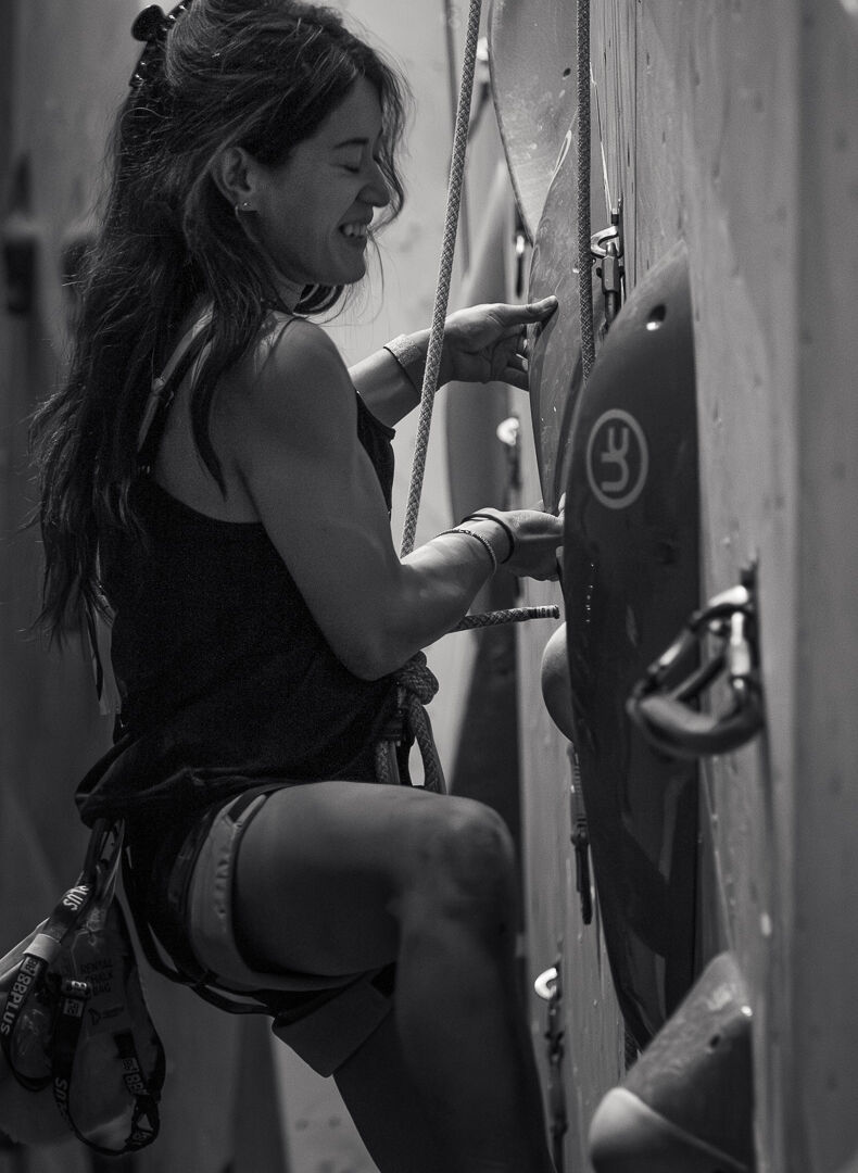 Ti Schwarz pulls on the underside of a climbing hold and bursts into a smile during the Beast Fingers League (BFL) climbing competition at Longmont Climbing Collective in August 2026. (Photo by Harley Parsons)